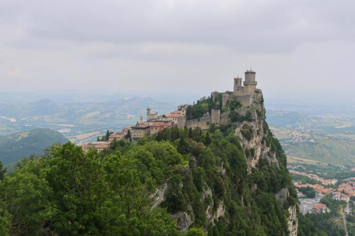 Blick vom zweiten Turm Cesta auf den markanten ersten Turm Guaita und die historische Kulisse der Altstadt von San Marino mit dem markanten Regierungspalast Palazzo Pubblico